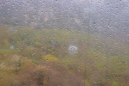 Raindrops on a window blur the colorful landscape outside on a quiet, rainy day.の写真素材