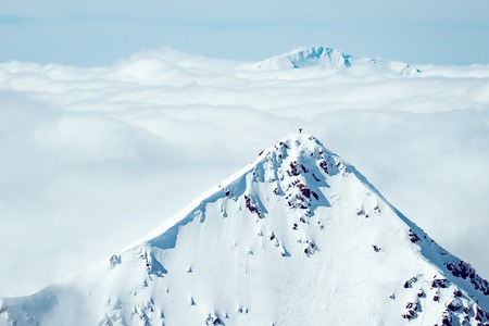A climber stanting on top of a distant mountain in winterの写真素材