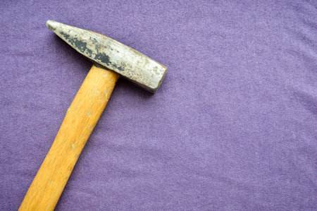 Old hammer with a wooden handle on a background of purple cloth.