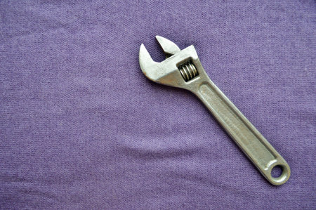 Metal, iron, shiny, adjustable wrench on a background of purple cloth. Bench tools.
