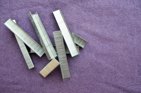 Iron, metal, silvery construction staples stacked in heap on a purple background.