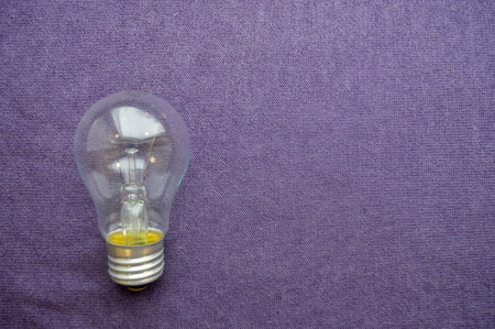 A round, ordinary, non-economical incandescent bulb with a transparent socle background of purple...