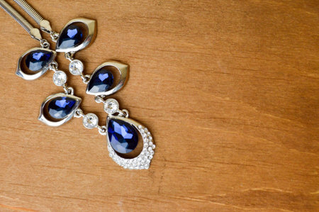 Female silver jewelry with blue gems, diamonds on a brown, wooden background in the upper left...