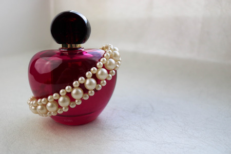 Pink beautiful glass transparent bottle of female perfume decorated with white precious pearls and place for a simple text on a light white background.の写真素材