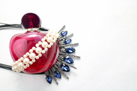 Pink beautiful glass transparent bottle of female perfume decorated with white drab pearls and blue diamonds and place for a simple text on a light white background.の写真素材