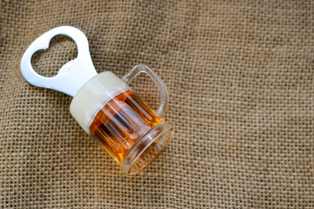 Yellow metal opener for bottles with a handle in the form of a glass of beer against the texture of a brown old linen cloth of linen with a coarse perpendicular interlacing of the fibers of the fabricの写真素材