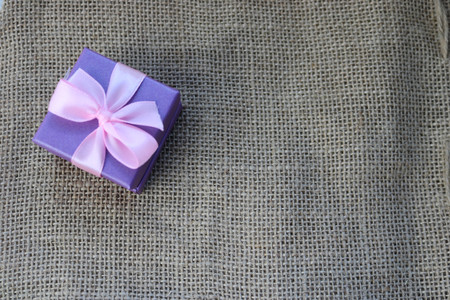Violet gift beautiful festive cardboard small gift box with a pink bow on a background of brown linen, self-made, unbleached cloth from vegetable fibers, mitkal.の写真素材