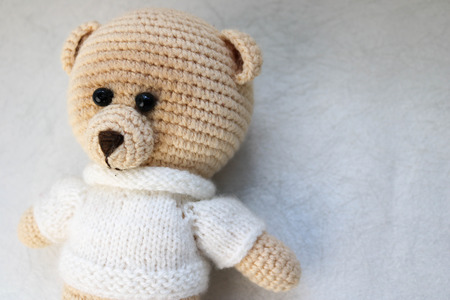 A knitted homemade beautiful cute little bear in a white sweater with black eyes, a soft toy tied with beige large threads on a light white background. The background.の写真素材