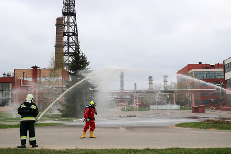 Professional firefighters in orange fire-resistant suits in white helmets with gas masks are testing fire hoses and fire guns to extinguish a fire at a chemical refinery.のeditorial素材