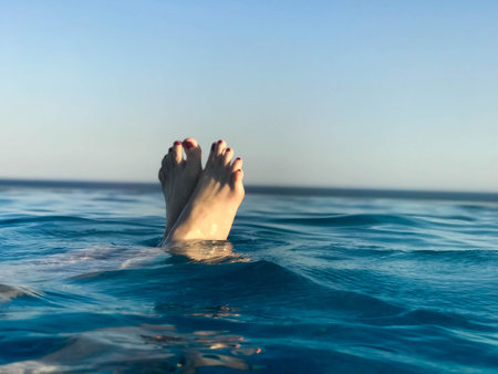 Beautiful blue wet water with waves and female feet, feet with a red pedicure on the background of...