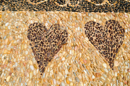 The texture of the stone wall, the road from small round and oval stones with abstracted lines of patterns of two hearts sandy seams of natural old yellow black brown. The background.の写真素材