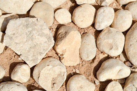 Texture of a stone wall, roads from large round and oval stones with sand with seams of natural old...