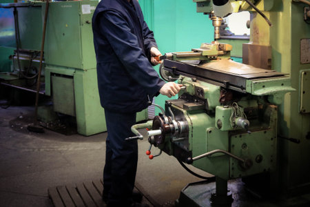 A male worker works on a larger metal iron locksmith lathe, equipment for repairs, metal work in a...