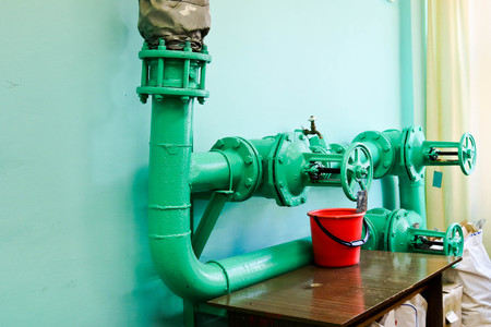 Leaking faulty valve, fitting on the pipeline with a bucket under it in the factory plant. Concept: repair of pipe and valve with available tools.の写真素材