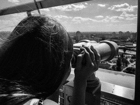 A beautiful girl looks at the landscape, a panorama of the city in the observation room, a pair of binoculars, a telescope with a bill acceptor on an observation deck in the open air.の写真素材