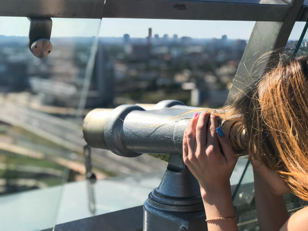 A beautiful girl looks at the landscape, a panorama of the city in the observation room, a pair of binoculars, a telescope with a bill acceptor on an observation deck in the open air.の写真素材