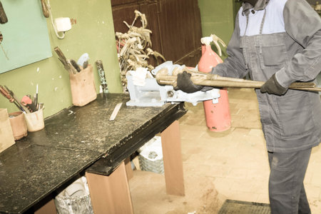 A man working on a large metal industrial vice with a huge gas wrench unscrews a nut on a red fire...
