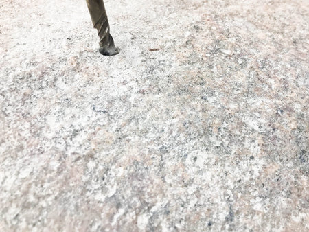 A sturdy, hard metal iron drill bit drills a hole in a large gray stone. Close view. The background.