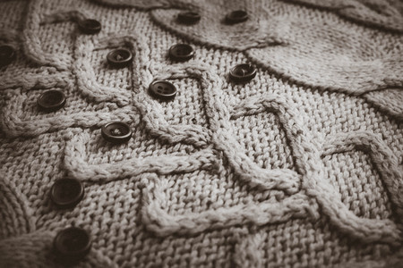 Beautiful texture of a soft warm natural sweater with a knitted pattern of yarn and black and white small round buttons. The background.の写真素材