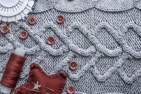 Beautiful texture of a soft warm natural sweater, fabrics with a knitted pattern and red small round...