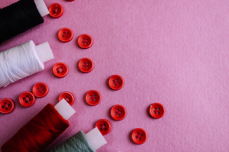 Beautiful texture with lots of round red buttons for sewing, needlework and skeins of spools of thread. Copy space. Flat lay. Pink, purple background.の写真素材