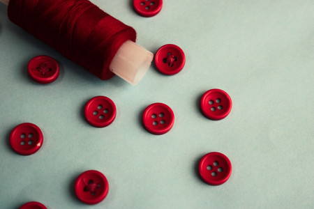 Beautiful texture with lots of round red buttons for sewing, needlework and a coil of thread. Copy space. Flat lay. Blue background.の写真素材