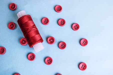 Beautiful texture with lots of round red buttons for sewing, needlework and a coil of thread. Copy space. Flat lay. Blue background.の写真素材