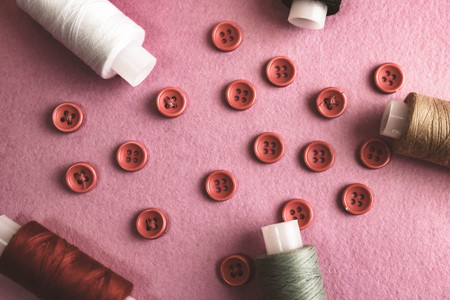 Beautiful frame with a lot of round red buttons for sewing, needlework and skeins of spools of thread. Copy space. Flat lay. Purple pink background.の写真素材