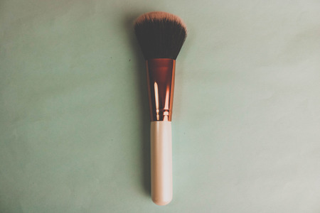 A beautiful soft brush for make-up from natural nap for beauty targeting and applying a tonal base with a wooden pen and copy space on a green background.の写真素材