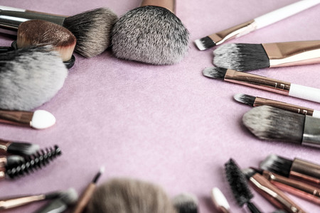 A frame from a set of beautiful different soft makeup brushes from natural lint for targeting beauty and applying a tonal base in a stand and copy space on a pink, purple background.の写真素材