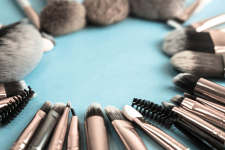 A frame from a set of beautiful different soft makeup brushes from natural lint for targeting beauty and applying a tonal foundation in a stand and copy space on a blue background.の写真素材