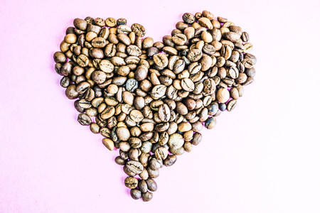 Beautiful texture in the shape of a heart from freshly roasted selected delicious saturated brown natural fragrant Arabica and Robusta coffee beans. Copy space, flat lay, pink purple background.の写真素材