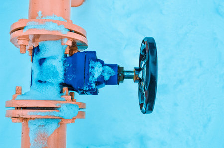 Industrial shut-off regulating protective pipe fittings. Black valve for opening, closing on an iron orange metal pipe with flanges, studs, nuts against the background of white snow in winter.の写真素材