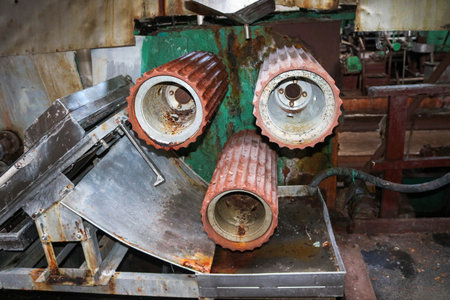 Large metal rollers rolls with teeth of the gears of the production line, a conveyor belt in the...