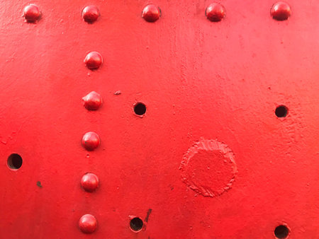 Red iron metal rough painted strong solid industrial wall with rivet holes and bolts. Background,...