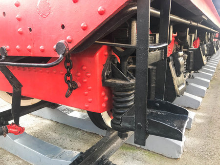 Large iron wheels of a red and black train standing on rails and suspension elements with springs of...