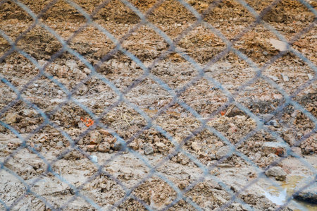 View of the brown earth through a metal wicker iron grid netting net. The background. Texture.