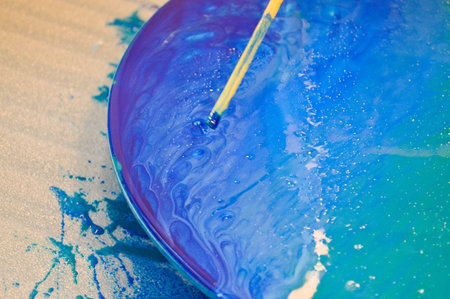 The process of creating a home-made trendy abstract modern pattern painted with a brush of acrylic blue multi-colored resin on a round wooden board.の写真素材