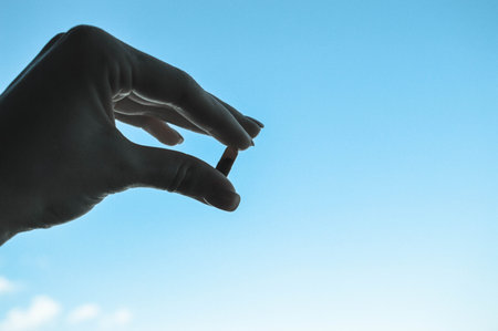 Beautiful female hand holds a medical pharmaceutical pill capsule from coronavirus covid-19 for the treatment of diseases and viruses on a blue sky background.の写真素材