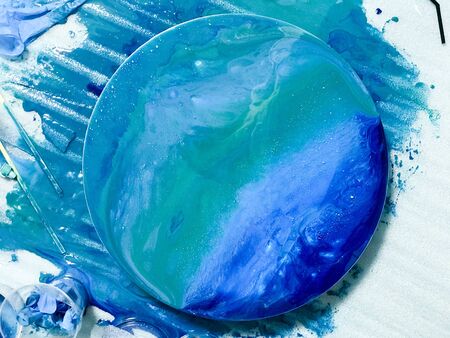 The process of creating a home-made trendy abstract modern pattern painted with a brush of acrylic blue multi-colored resin on a round wooden board.の写真素材