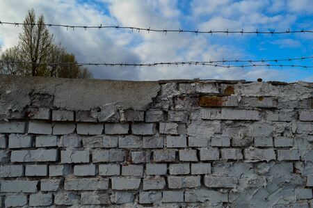 Beautiful white painted brick wall shabby old with cracks in the loft style with seams and barbed wire against the blue sky. Texture, background.の写真素材