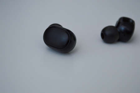 black small wireless headphones lie on a white surface. a device for listening to music in a macro-angle. beautiful stylish accessory. convenient music switching buttons.の写真素材