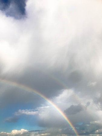bright rainbow on gray rainy sky. double rainbow, the manifestation of rain drops in different...