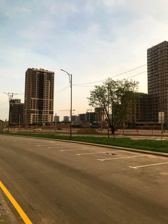 city panorama. tall glass houses stand along an asphalt road with a yellow stripe. near lampposts to...