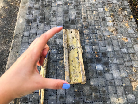 metallic yellow and rusty piece of metal lies on the asphalt. girl with blue manicure holds metal...
