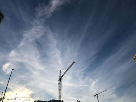 construction cranes stand against the background of a cloudy blue sky. construction site, house building equipment. builders erect tall houses from concrete blocks.の写真素材