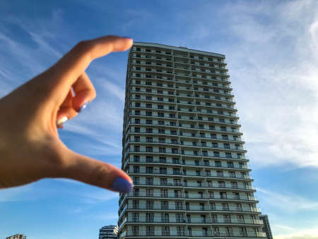 a tall white house made of aerated concrete. with panoramic glazing, in Arabic style with terraces. girl holding fingers, measuring the size of the house. blue creative manicure on nails.の写真素材