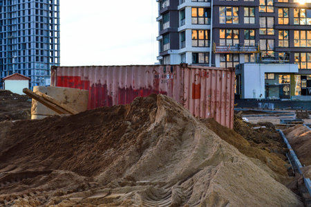 a large mountain of sand lies on a construction site in the city center. sand lies against the...
