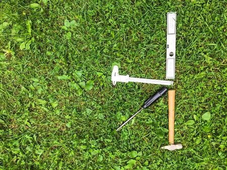 on the grass lies a hammer and a screwdriver, a level and others. K-shaped repair tools are laid out...