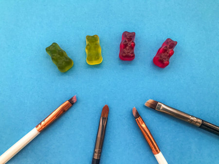 makeup brushes lie on a blue matte background next to the gummy bears. handwork. culinary...